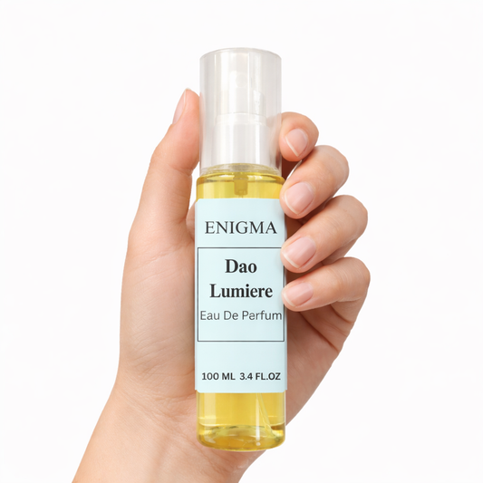 Hand holding a bottle of 'Enigma Dao Lumiere' eau de parfum against a white background